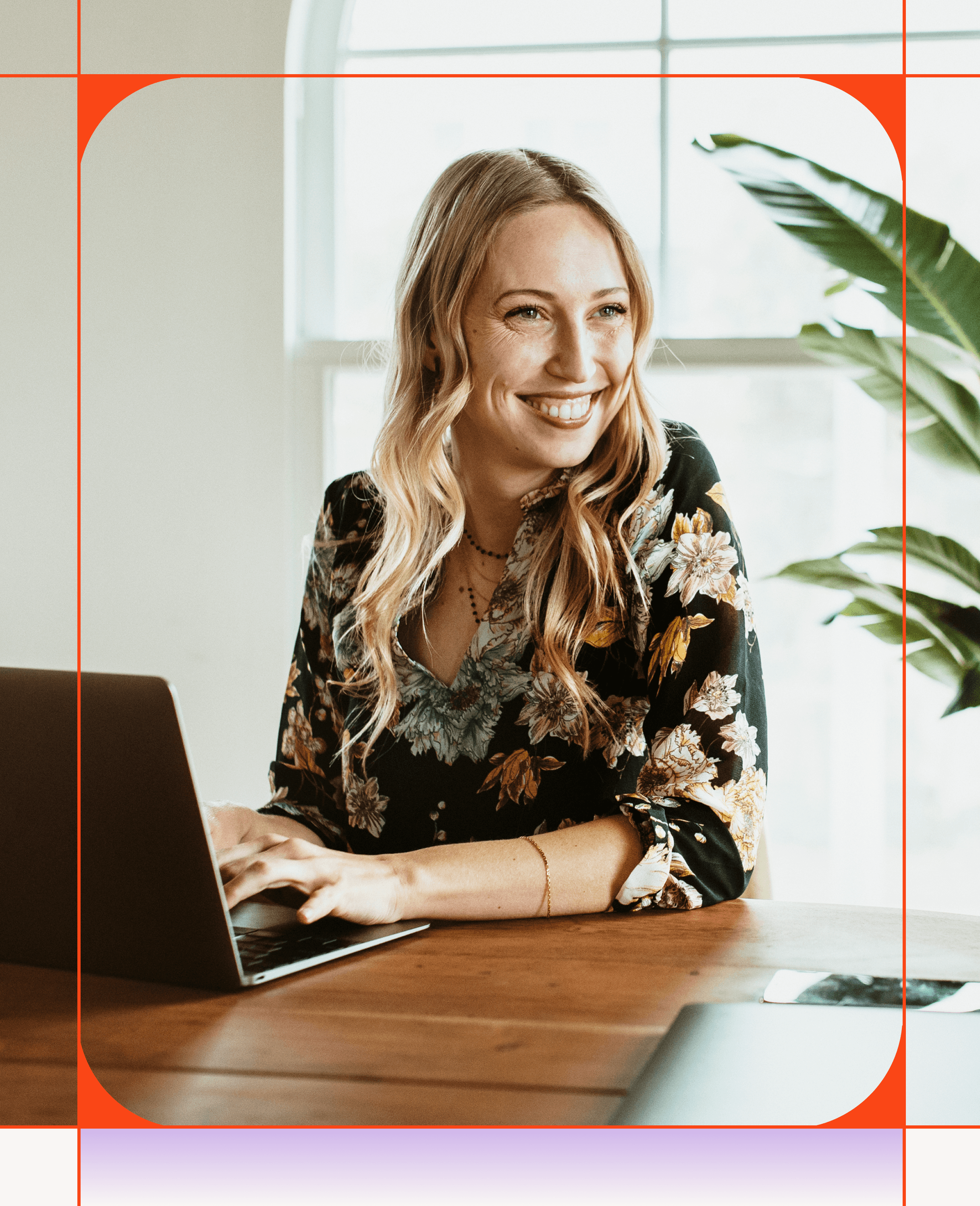Smiling blonde woman typing on a laptop at a wooden table.