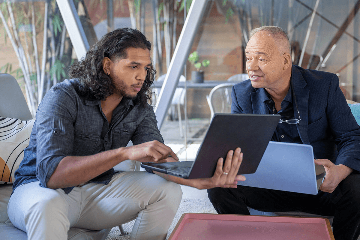 Two men discussing and working on laptops.